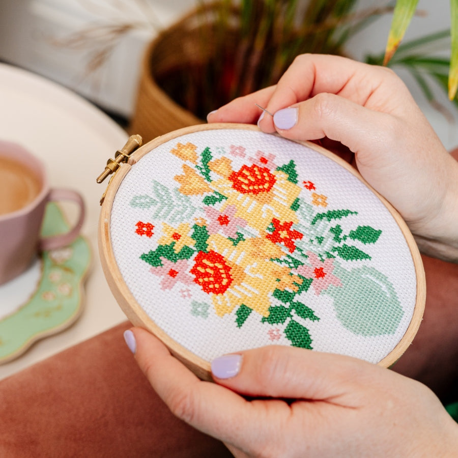 Person stitching floral cross stitch pattern in embroidery hoop