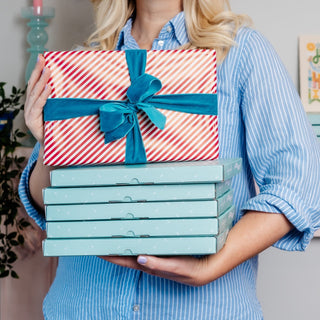 Woman holding stack of subscription boxes with one on top wrapped as present