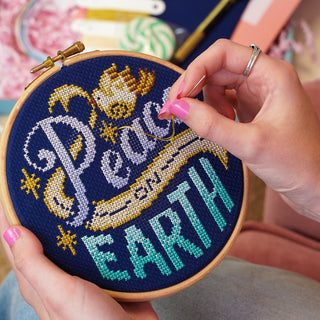 Person stitching 'Peace on Earth' cross stitch design