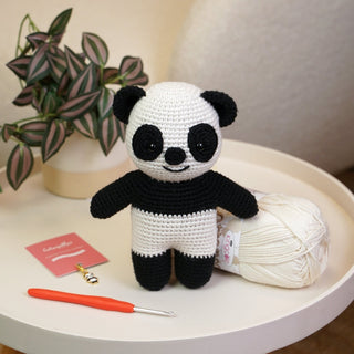 Crochet amigurumi panda toy on table with yarn, crochet hook and matching panda stitch marker