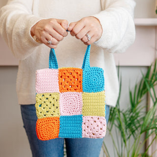 Person holding crochet tote bag made of different colour crochet squares