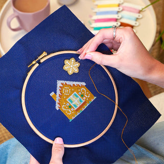 Gingerbread Lane Stitch-a-long stitching sneak peek sample in hand and cokkie needle minder