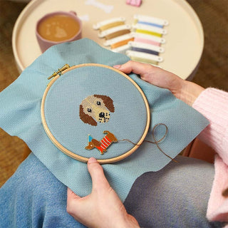 Person holding dog themed cross stitch design in embroidery hoop with Sausage Dog needle minder