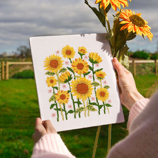 Person holding sunflower cross stitch pattern outside